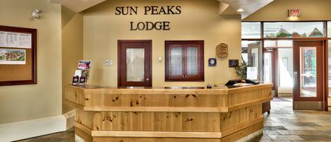 A reception desk at Sun Peaks Lodge with a wooden design, a bulletin board, and a sign indicating the exit.