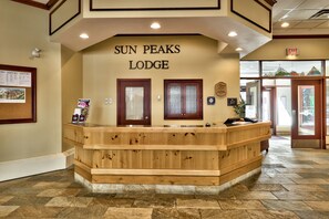 Mostrador de recepción en Sun Peaks Lodge con diseño de madera, un tablón de anuncios y un letrero que indica la salida.