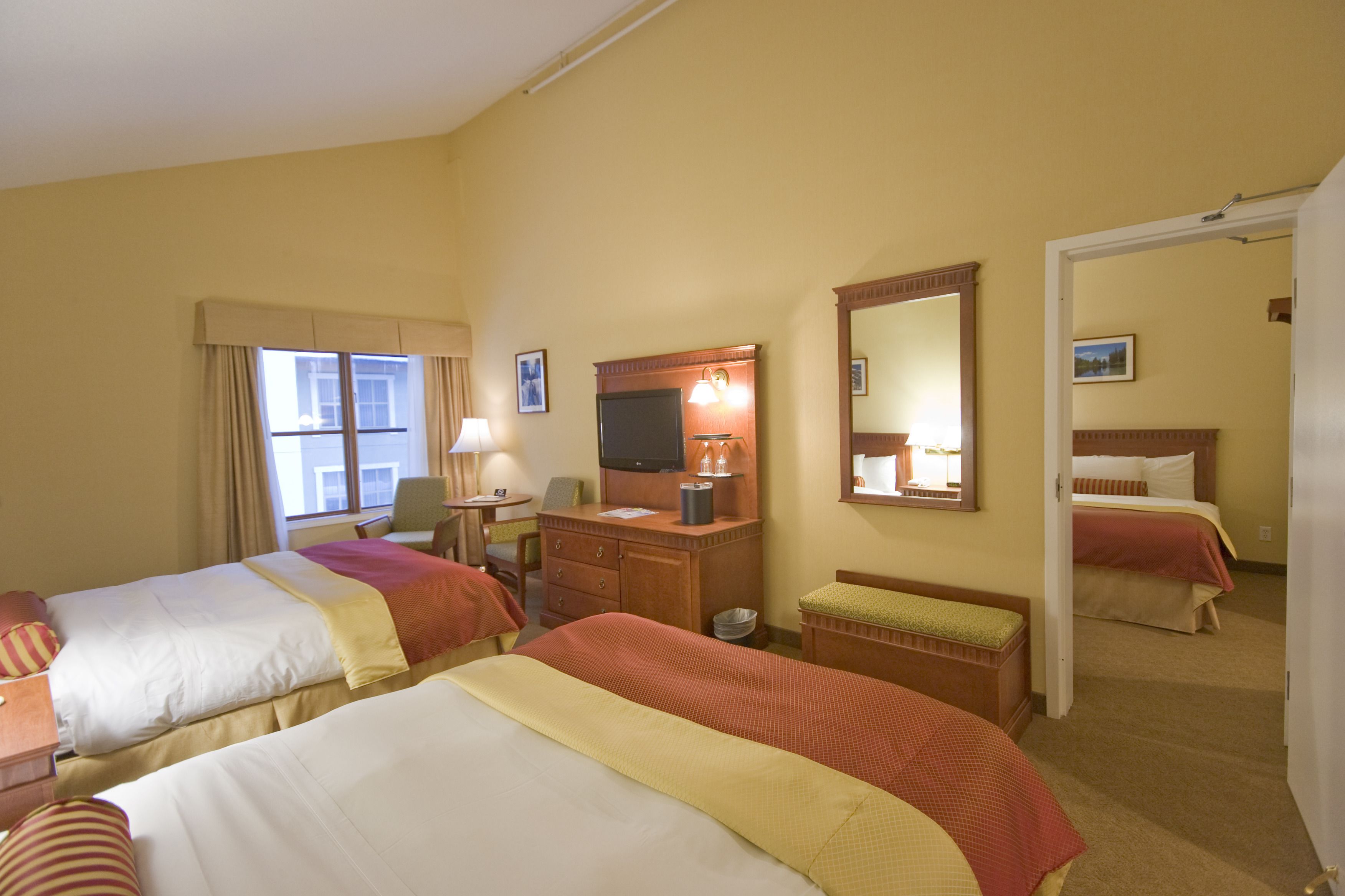 A hotel room with two beds, a desk, a television, and a bathroom visible through an open door.