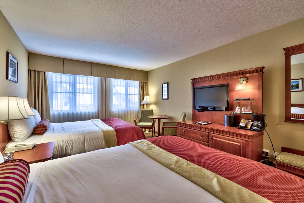 A hotel room with two beds, a desk with a lamp, a television, and a small table.
