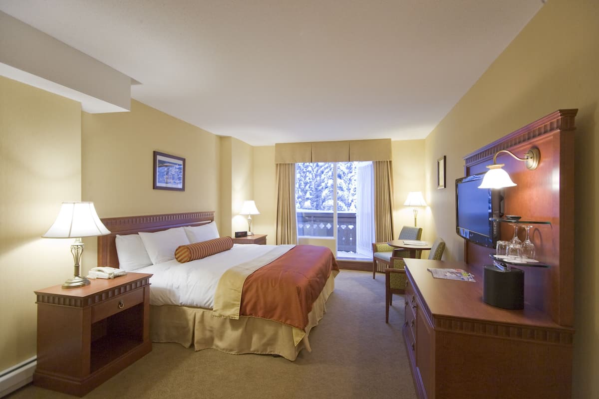 A hotel room with a large bed, two bedside tables with lamps, a desk with a chair, a television, and a window with curtains.