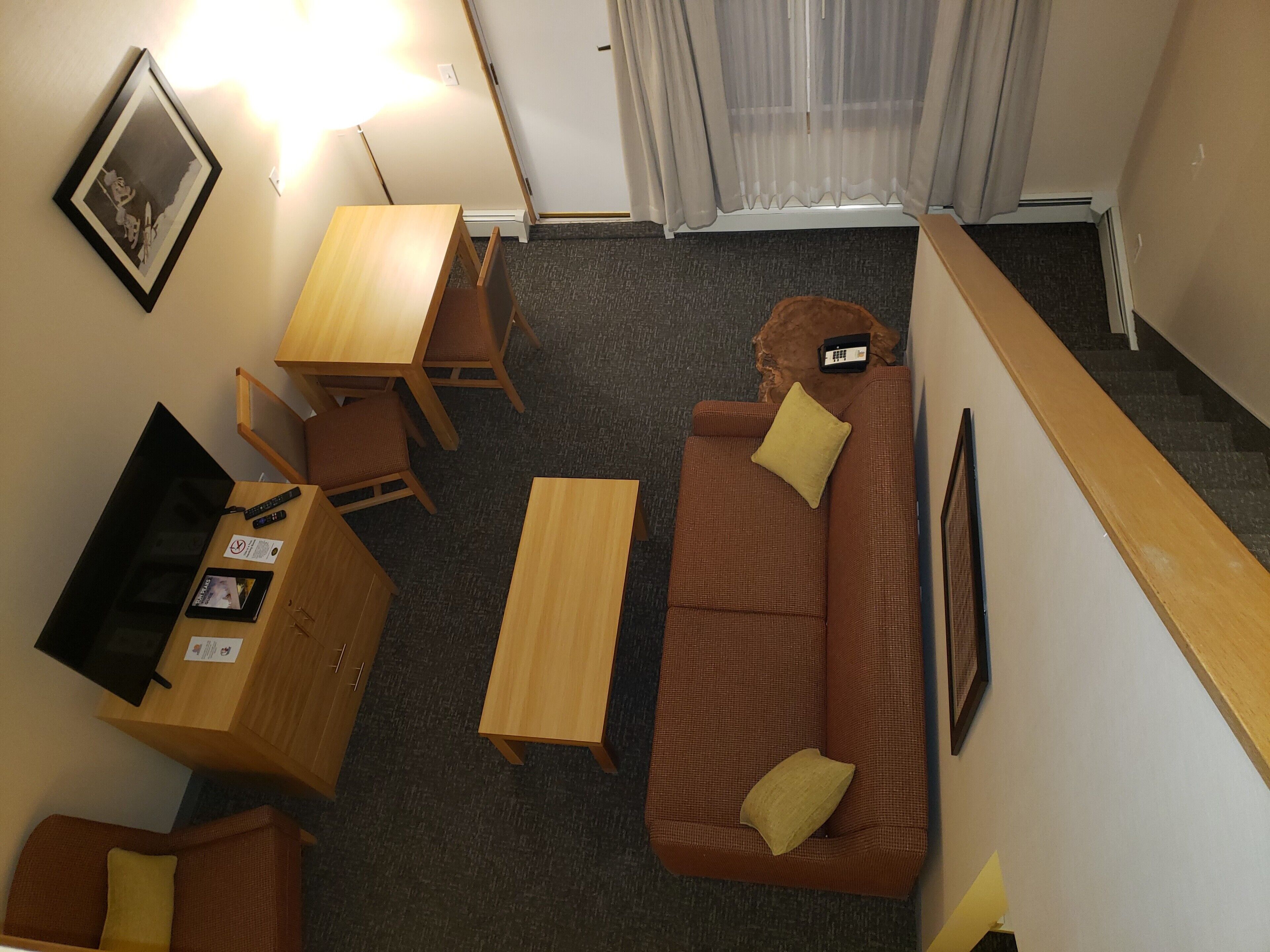 Un espace de vie compact comprenant un canapé marron, une table basse en bois, un petit bureau et un téléviseur.