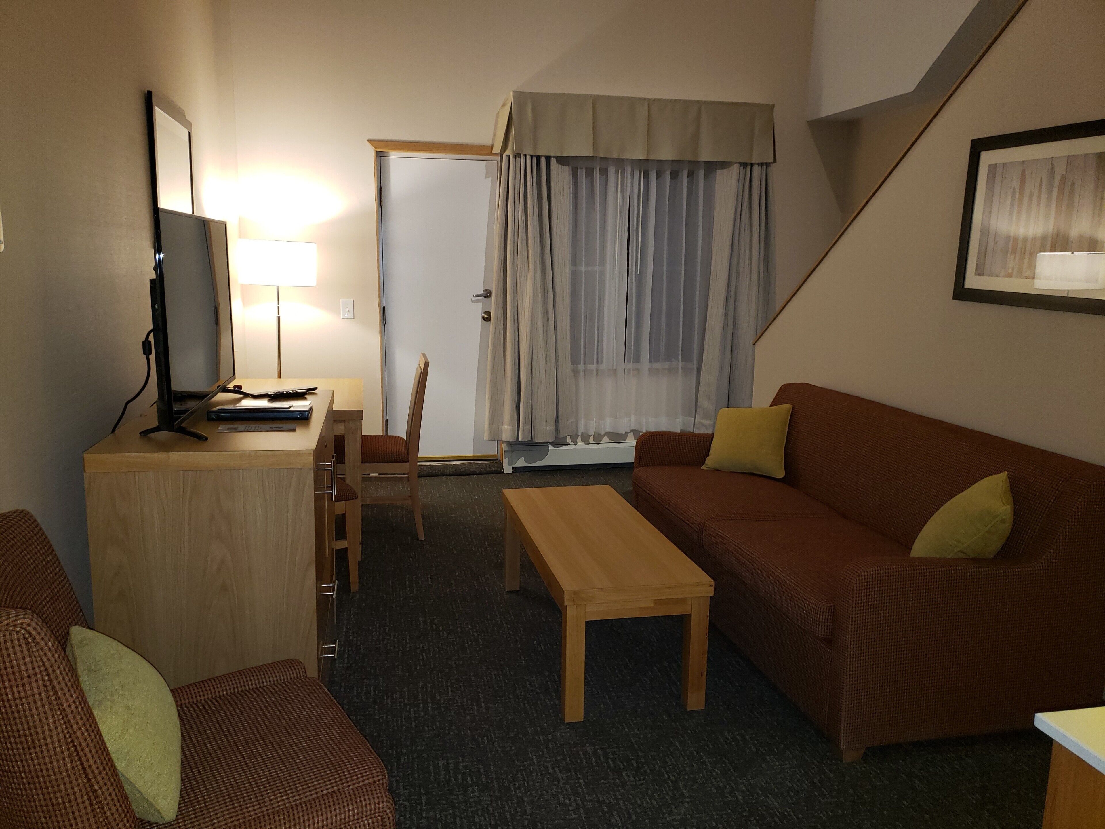 Un salon meublé comprenant un bureau en bois, une télévision, un canapé et un fauteuil.