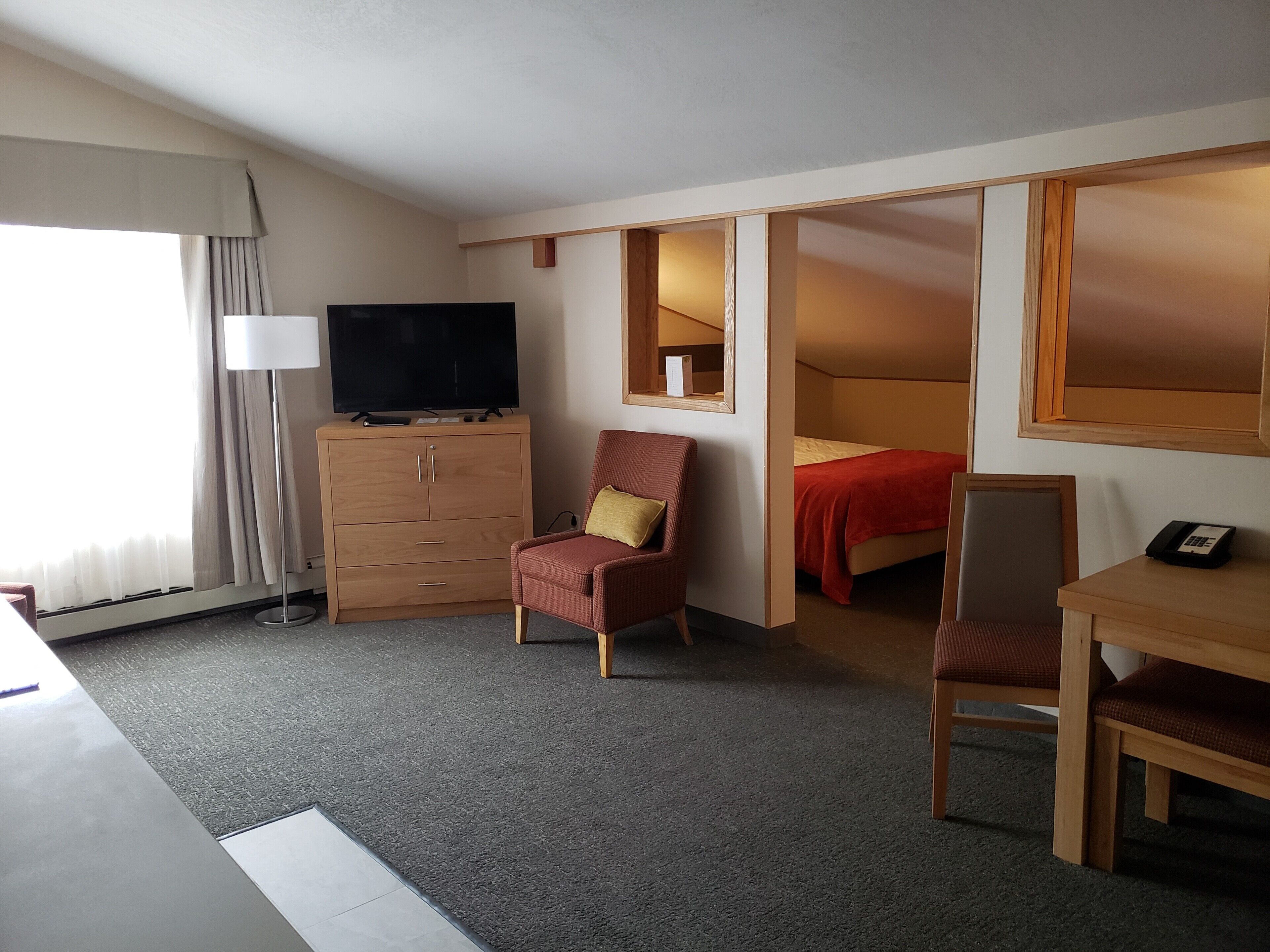 A hotel room with a TV, a desk, a chair, a bed, and a wardrobe.