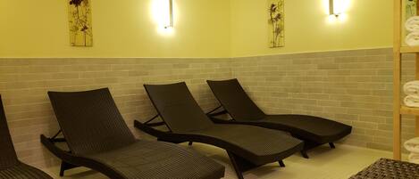 Cuatro sillones oscuros de mimbre alineados frente a una pared amarilla con dos luces fijadas a la pared.