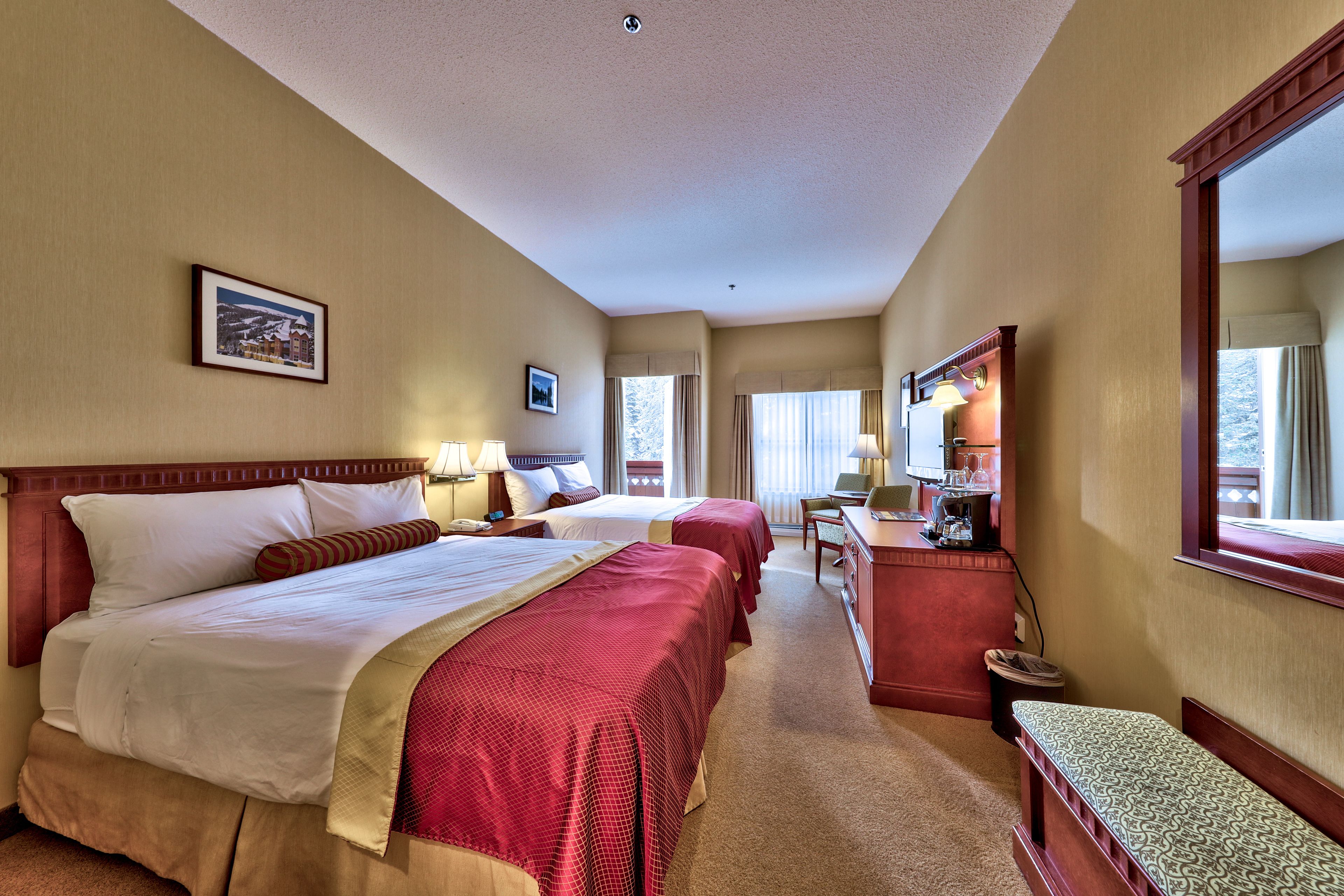 A hotel room with two beds, a desk, a chair, and a bench.