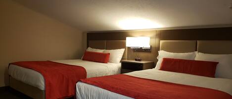 A hotel room with two beds, each with red and white bedding, a nightstand with a clock, and a wall-mounted light.