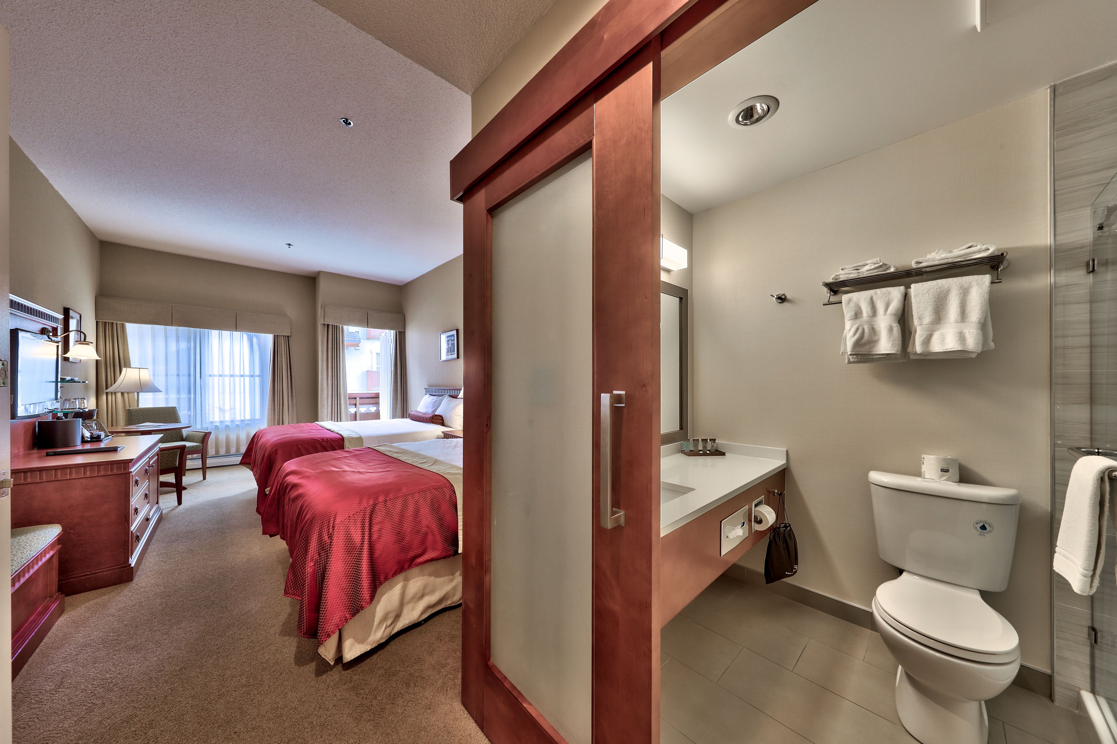 Ein Hotelzimmer mit Bett, Nachttischen, einem Schreibtisch und einem Badezimmer mit Toilette, Waschbecken und Dusche.