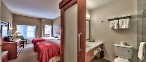 Ein Hotelzimmer mit Bett, Nachttischen, einem Schreibtisch und einem Badezimmer mit Toilette, Waschbecken und Dusche.