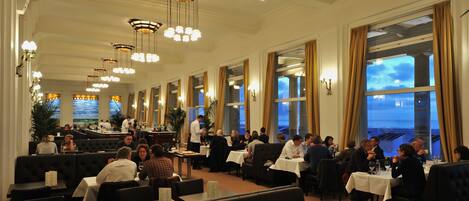 Ein geräumiges Restaurant mit hohen Decken, Kronleuchtern und großen Fenstern mit Meerblick.
