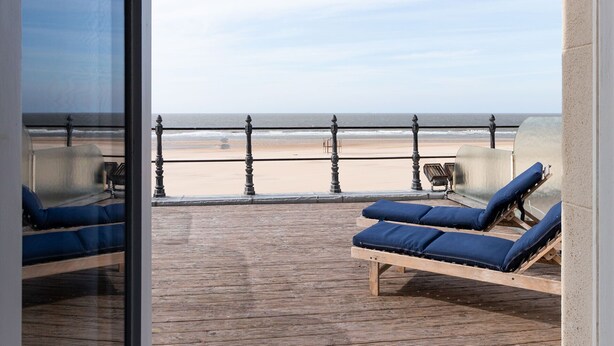 A balcony with two sun loungers and a table, overlooking a beach with a railing. - Thermae Palace Hotel (Ostend)