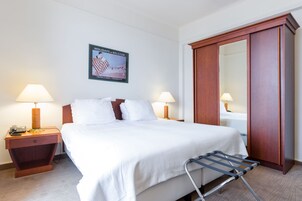 A hotel room with a large bed, two bedside tables with lamps, a wooden wardrobe, and a poster on the wall.