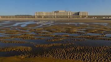 A beachfront hotel with a long pier extending into the water, sandy beach, and clear sky.