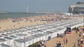 A beach with numerous white tents arranged in rows, a pier in the background, and a large building with a sign.