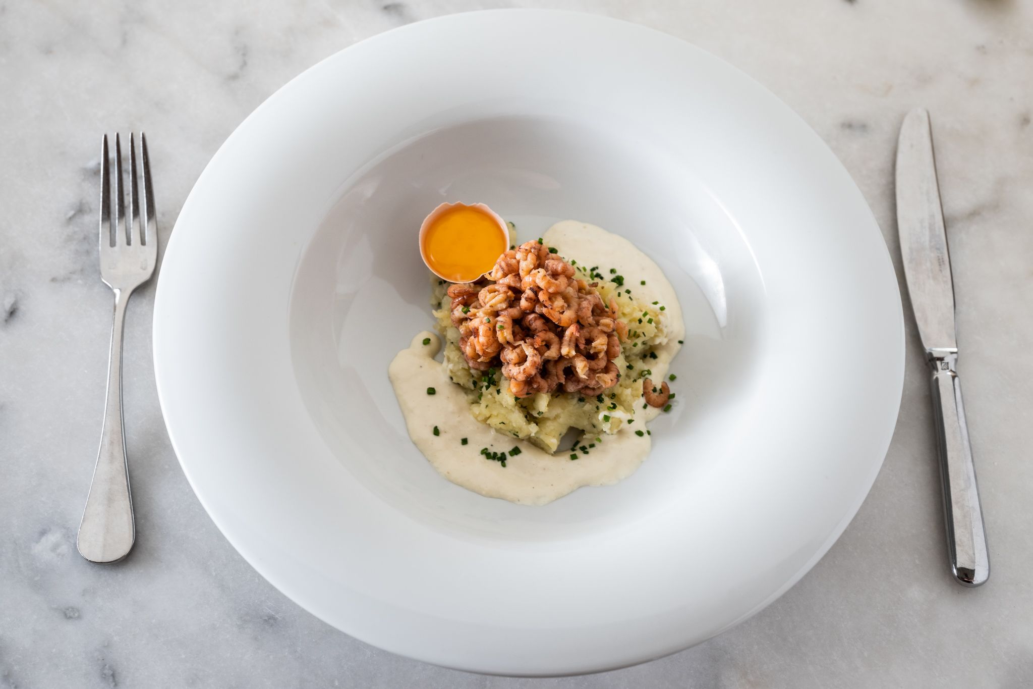 A white plate with a creamy dish, walnuts, and a small egg yolk on a marble surface.