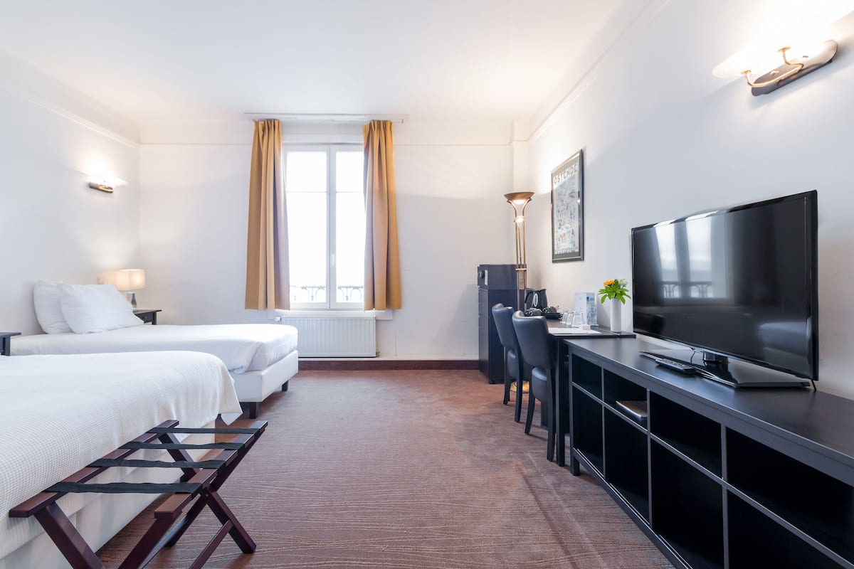 A hotel room with two beds, a television, a desk, and a window with curtains.