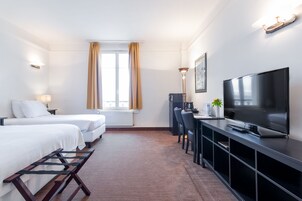 Habitación de hotel con dos camas, televisor, escritorio y ventana con cortinas.