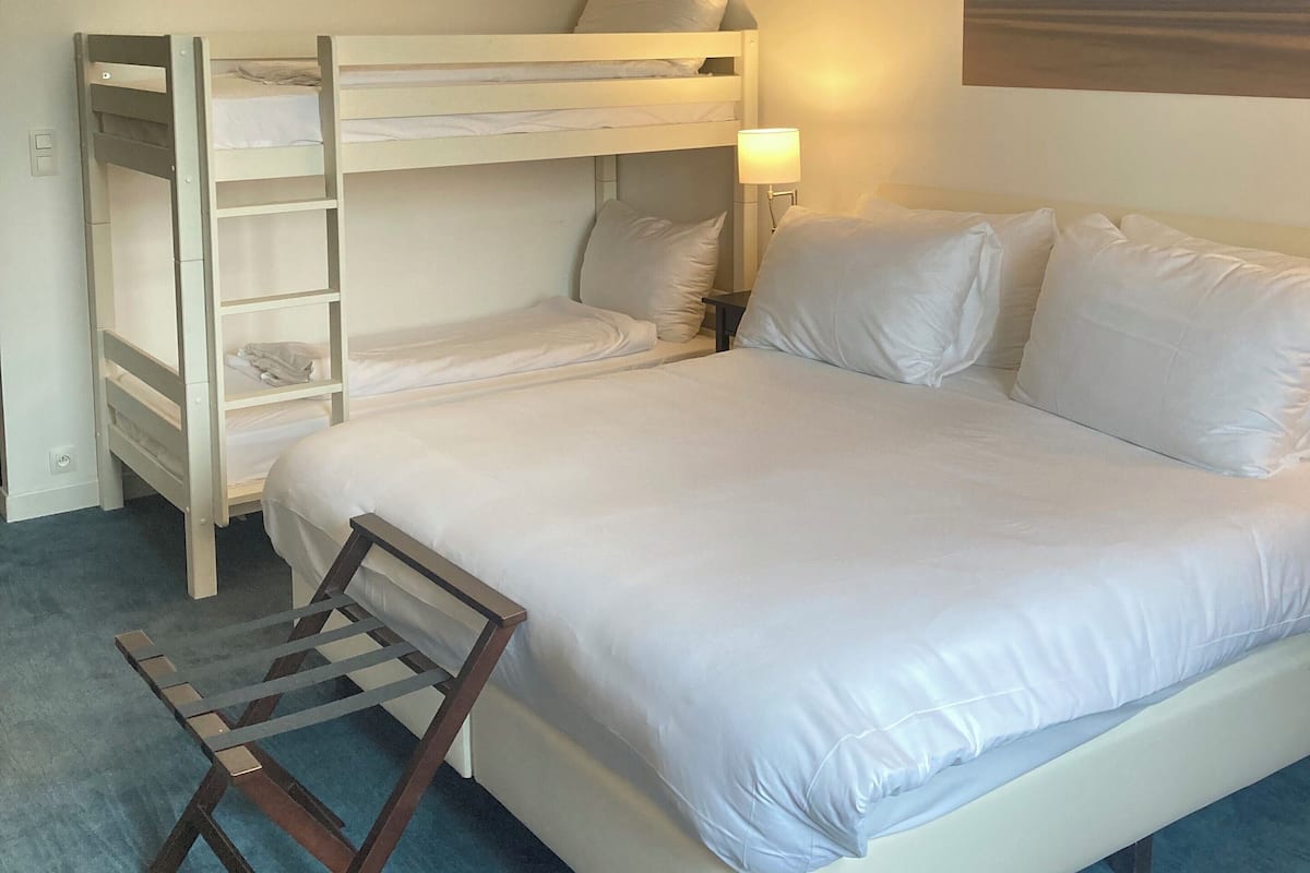 A hotel room with a bunk bed, a single bed, a desk, and a nightstand.