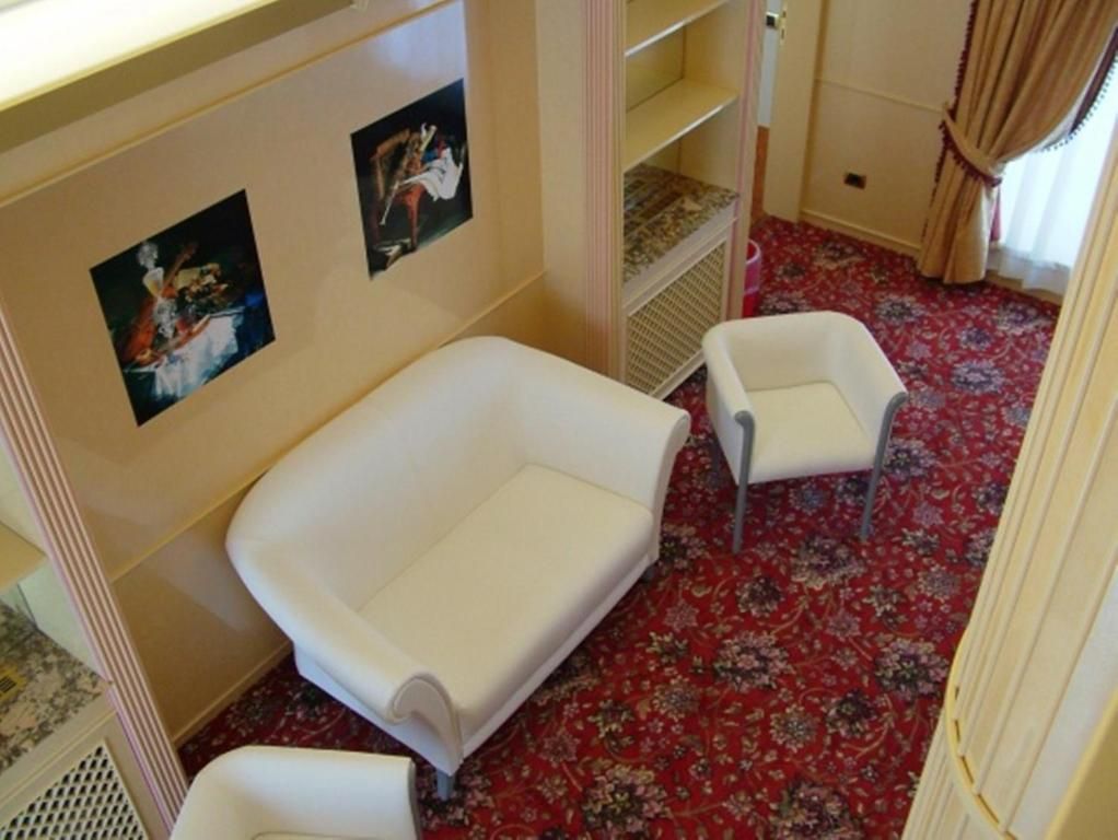 A room with a large white sofa, a smaller white armchair, and a patterned carpet.