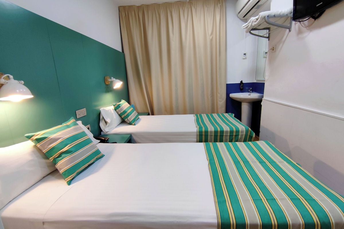 A hotel room with two beds, a bathroom with a sink, and a curtain.