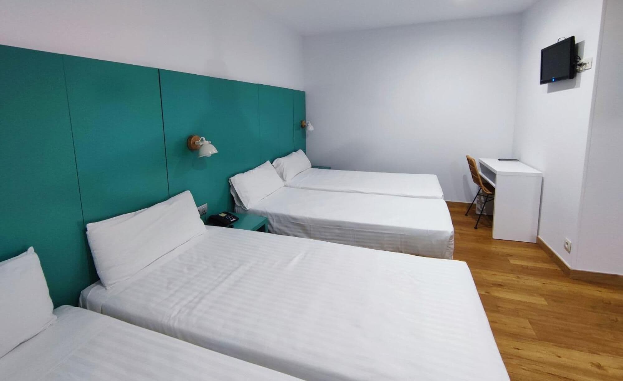 Ein Zimmer mit drei Einzelbetten, einem Schreibtisch und einem Stuhl.