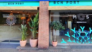 The storefront of BCN PORT with a clear glass facade, potted plants, and the logo 'MOS BIKINI & Bikinis' visible. - Yomo Hostal BCN Port (Barcelona)
