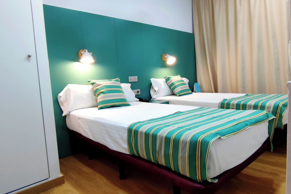 A hotel room with two beds, each with striped bedding and matching pillows. There are wall-mounted light fixtures above each bed.
