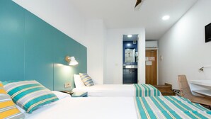A hotel room with two beds, a desk, a chair, a bathroom visible through an open door, and a wall-mounted light fixture. - Yomo Hostal BCN Port (Barcelona)