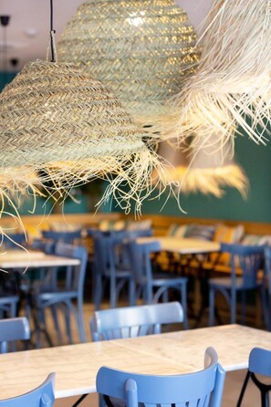 Interior de un restaurante con mesas y sillas redondas, y lámparas colgantes de tejido.