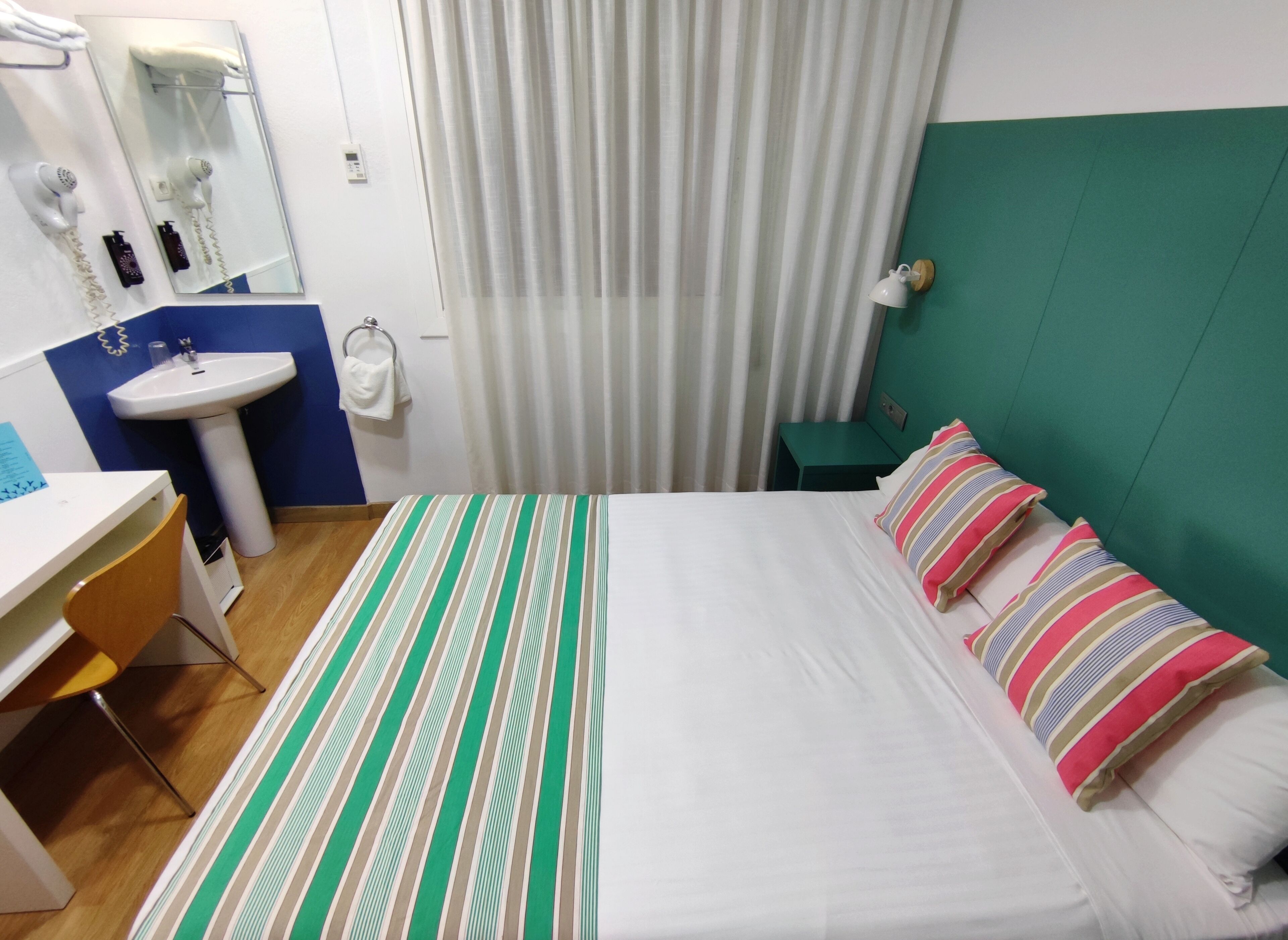 A hotel room with a bed, a desk, a sink, and a mirror.