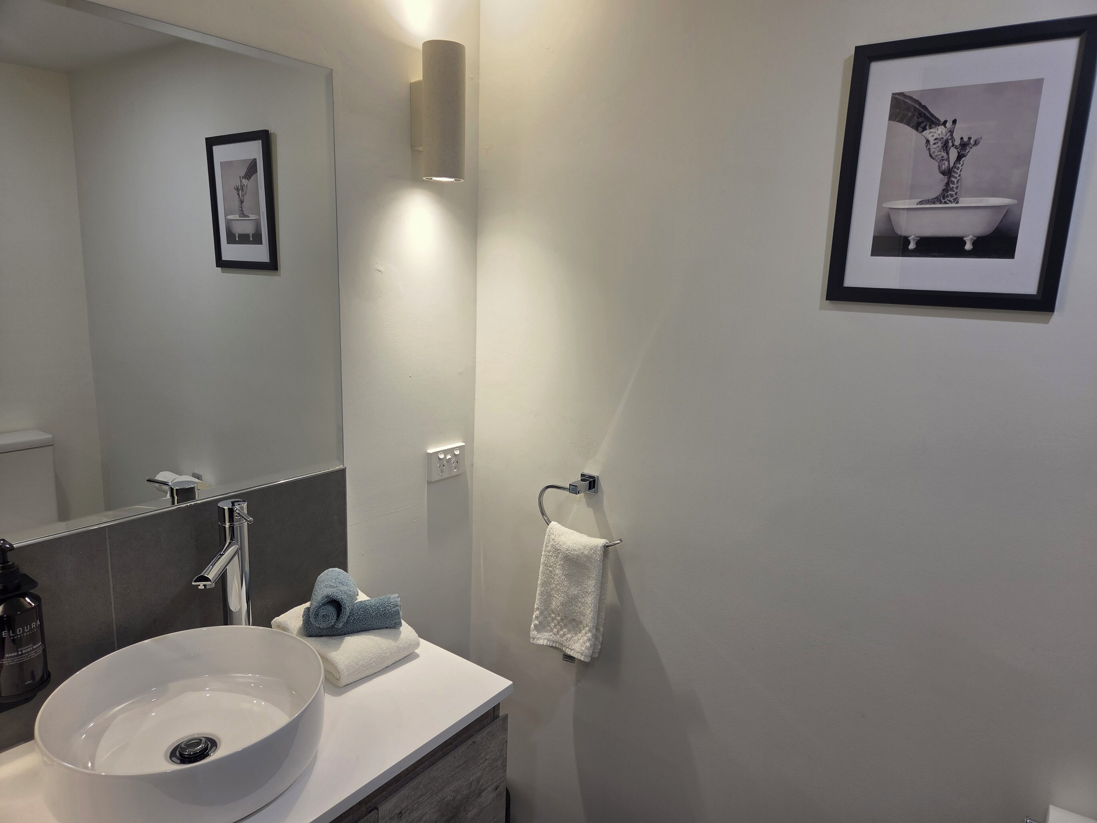 Un baño moderno con un espejo grande, un lavabo blanco y un cuadro en la pared.