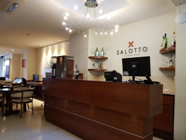 A reception desk with a chandelier, a coffee machine, and a computer. There are chairs and a table in the background. - Villaggio Hotel Boutique (Mendoza)
