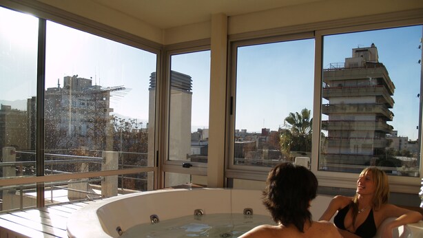 A hot tub with a city view, large windows, and a wooden deck. - Villaggio Hotel Boutique (Mendoza)