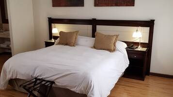 Una cama bien hecha con sábanas blancas y dos almohadas, suelo de madera y dos mesitas de noche con lámparas.