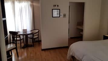 Quarto de hotel com cama, pequena mesa com cadeiras, janela com cortinas e porta para um banheiro.