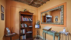 Een kamer met een houten boekenkast, een tafeltje met kantklosje, een spiegel met decoratieve lijst en een wand met een fotolijst.