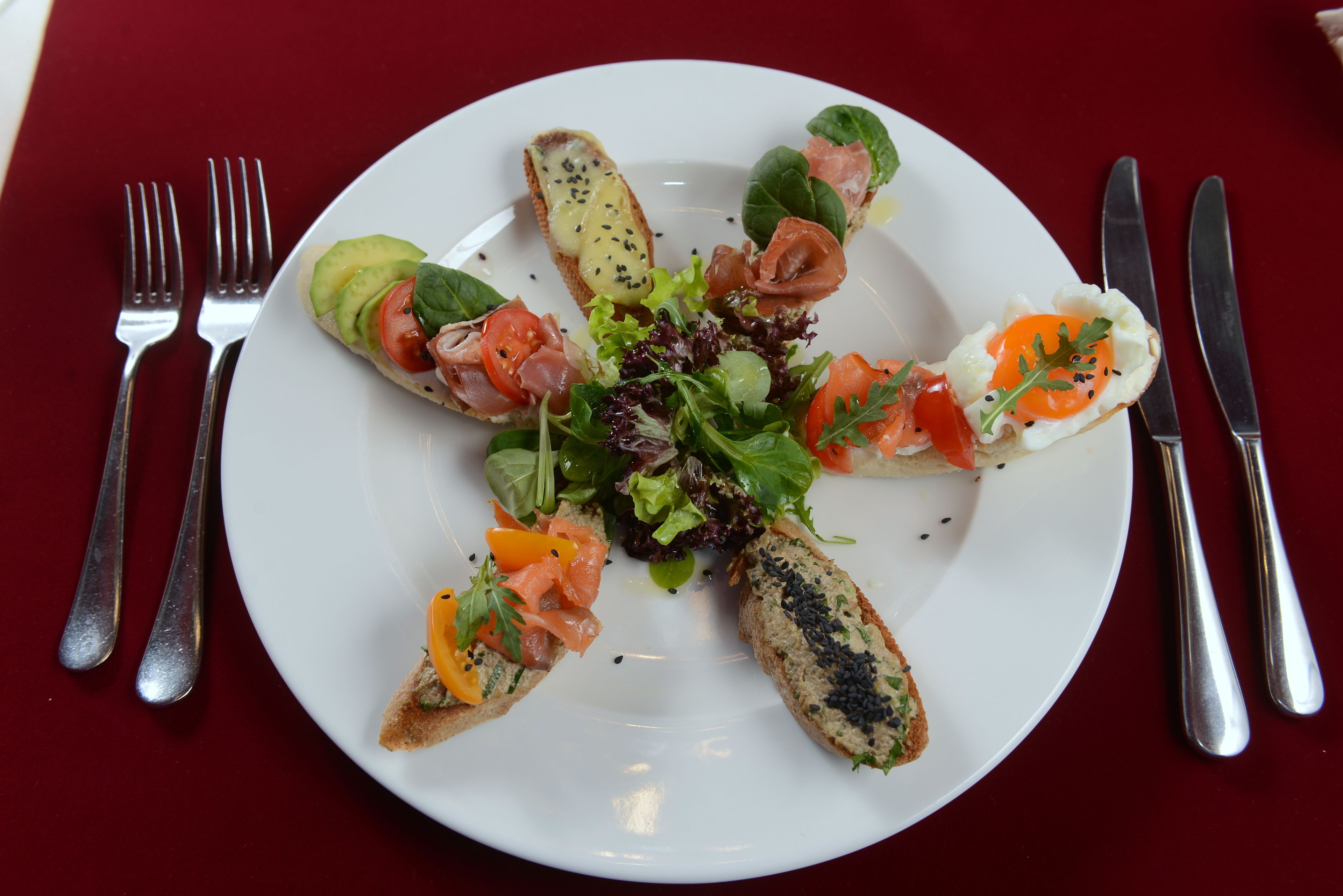 A white plate with various food items arranged on a red tablecloth.