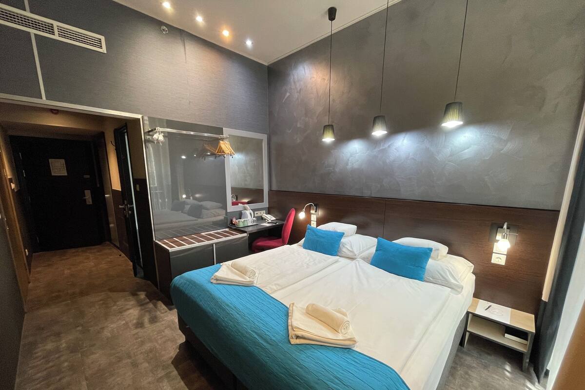 Une chambre d’hôtel moderne avec un grand lit, un bureau avec une lampe, un miroir et une armoire.