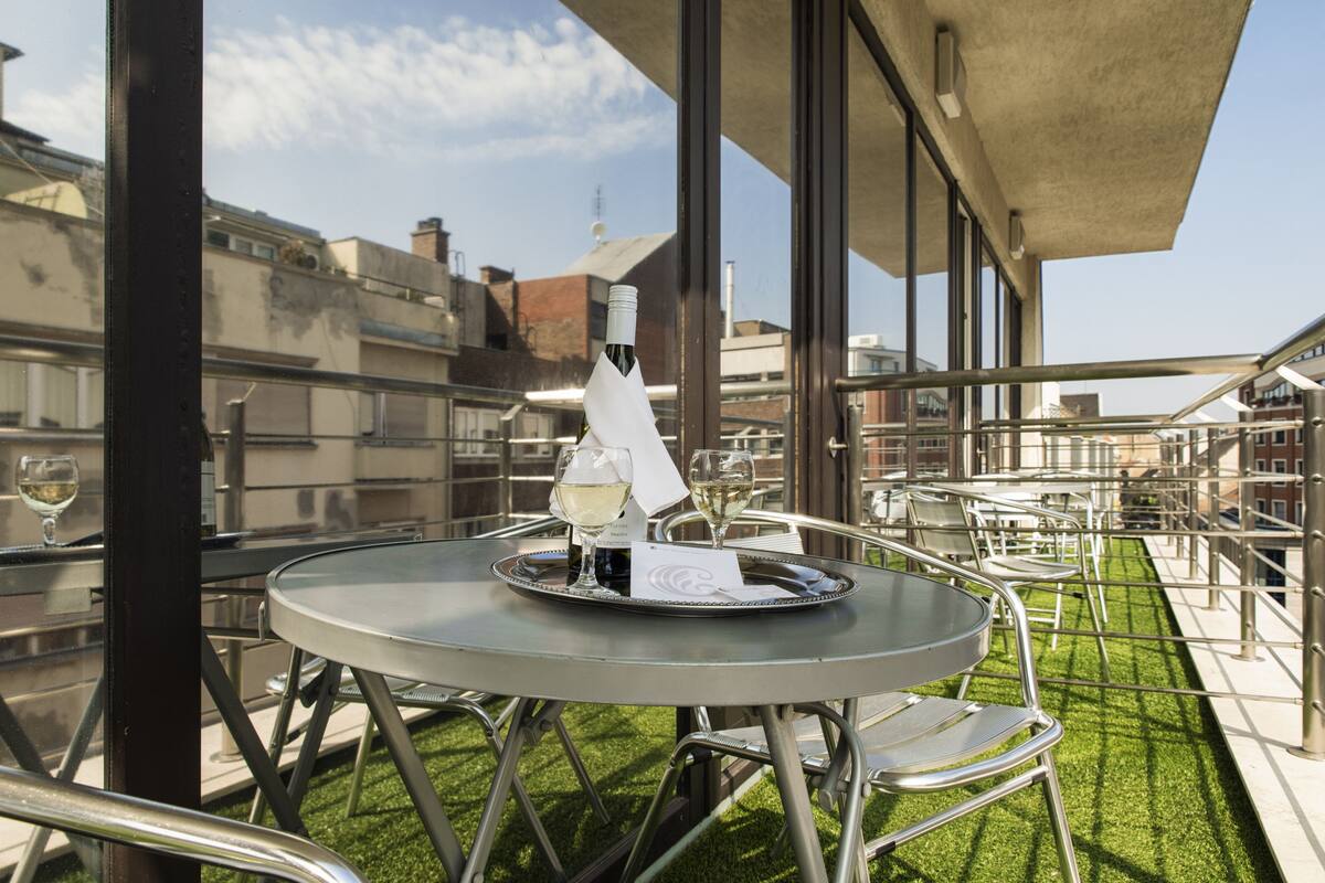 Une terrasse sur le toit avec une table ronde, des chaises et une bouteille de vin.