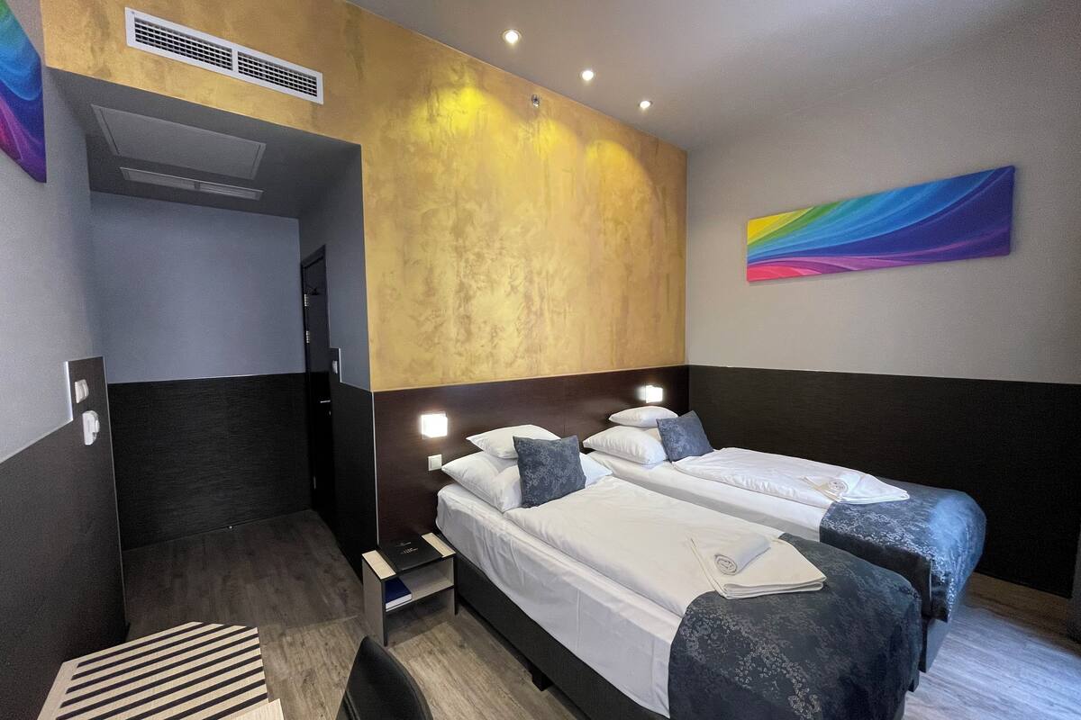 Une chambre d’hôtel avec deux lits, un espace douche et une peinture abstraite aux couleurs vives accrochée au mur.