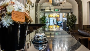 A hotel reception area with a polished reception desk, a decorative vase with flowers, and a chandelier. - Carat Boutique Hotel (Budapest)