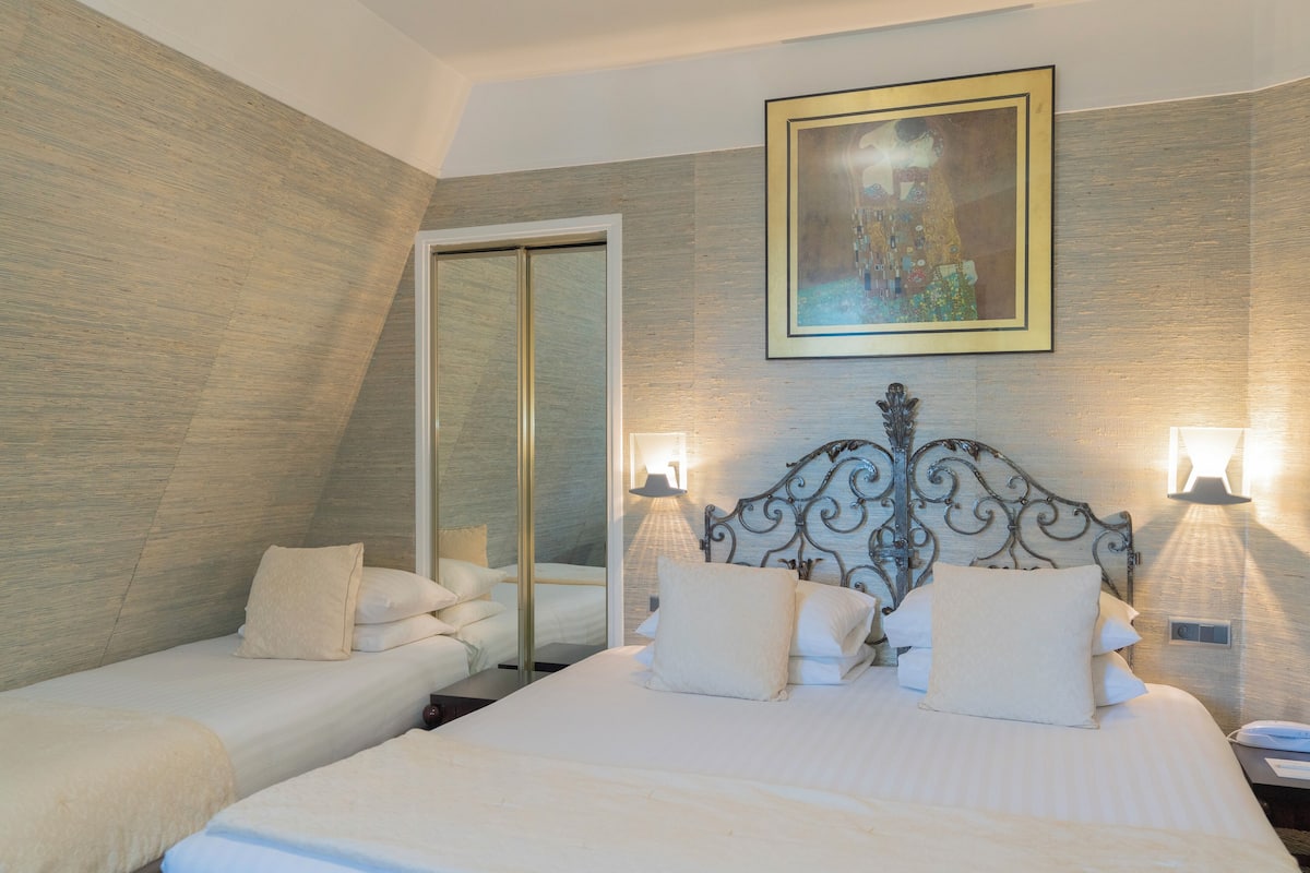 A hotel room with a large bed, two smaller beds, a mirror, and a painting on the wall.