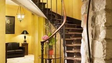 Un escalier avec une main courante en bois et une rampe noire, menant à un palier où se trouvent un canapé noir et une lampe.