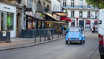 A street with a blue vintage car, storefronts including a burger restaurant, and a HSBC bank.