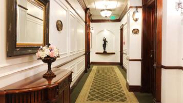 A hallway with a green patterned carpet, a wooden console table with a vase of flowers, a mirror, and a statue on a shelf.