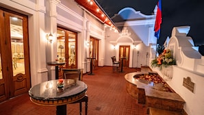 A well-lit outdoor patio area with a round table and chairs, a fountain with flowers, and a flag. - Hotel Plaza Grande (Quito)