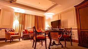A hotel room with a dining area, a sofa, two armchairs, a chandelier, and a large mirror.
