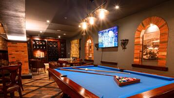 A pool table in a room with a bar area, brick walls, and a mounted television.