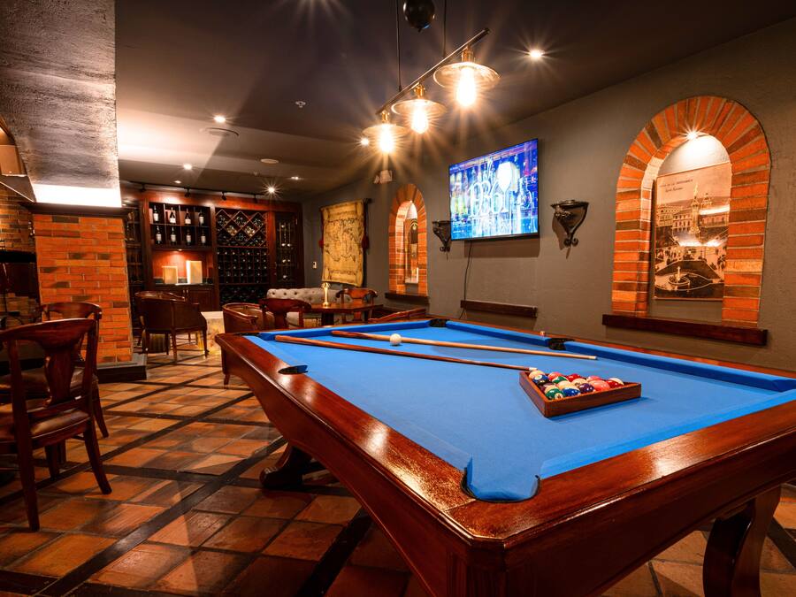 A pool table in a room with a bar area, brick walls, and a mounted television.