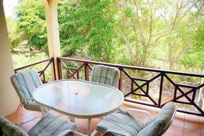 A balcony with a glass table and four chairs, surrounded by a wooden railing, overlooking a lush garden. - Paradise Cove Resort (Cove Bay)